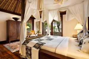 a bedroom with a large bed with white curtains at The Oberoi Beach Resort, Lombok in Tanjung
