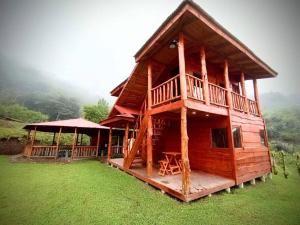 a large wooden cabin with a porch and grass at Finca La Gozadera in Jardín