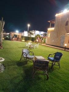 3 Stühle und ein Tisch in einem Garten in der Nacht in der Unterkunft فيلا للايجار في مارينا 4 حمام سباحة خاص in El-Alamein