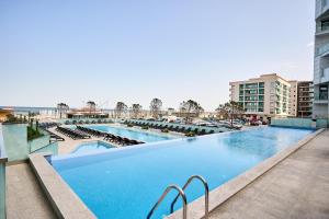 une grande piscine avec des chaises et des bâtiments dans l'établissement La Mer by Infinity Resort & SPA, à Mamaia Nord – Năvodari