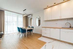 a kitchen with white cabinets and a table with chairs at Apartament Mierzeja LUX Baltic Garden in Sztutowo