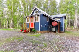 ein blaues Haus mit einer roten Tür im Wald in der Unterkunft Charming Alaska Vacation Rental with Gas Grill! in Talkeetna