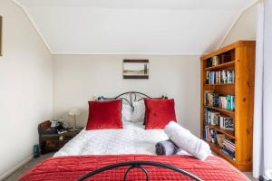 een slaapkamer met een bed met rode kussens en een boekenplank bij Quiet and cosy in Waikanae