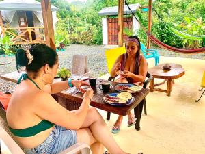 zwei Frauen sitzen an einem Tisch und essen Essen in der Unterkunft Mi casa es tu casa Glamping in Capurganá