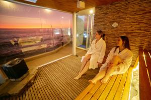 two women sitting on a bench in a room with a window at Maressenza Night Spa in Viña del Mar
