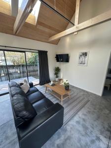 a living room with a black leather couch and a table at Modern Two bedroom Oasis in Whangamata