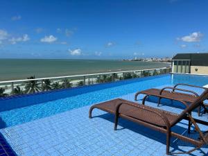 a swimming pool with two benches and a view of the beach at Flat Beira Mar de Intermares in Cabedelo