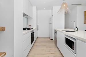 a white kitchen with white counters and a wooden floor at Collaroy Beachfront Escape - New Listing in Collaroy