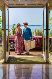 Ein Mann und eine Frau gehen mit einem Koffer in ein Auto. in der Unterkunft Hotel Villa Florida & Suite Apartments in Gardone Riviera
