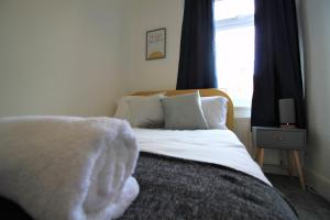 a bedroom with a bed with white sheets and a window at Westbourne - Spacious 4 bed flat with free parking in Gateshead