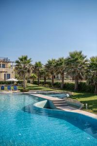 a swimming pool with blue chairs and palm trees at Calmaliving Seaside apartments with pool in Gerani Chanion