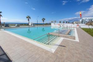 a large swimming pool with palm trees and the ocean at Ático frontal al mar en Duna Beach con vistas in Torrox Costa