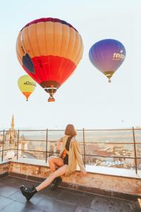 Una mujer sentada en una cornisa con dos globos aerostáticos en Peristyle Cave Cappadocia- Special Class, en Uchisar