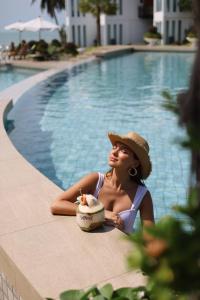 a woman in a hat sitting next to a swimming pool at Vannee Golden Sands Beachfront Resort in Haad Rin