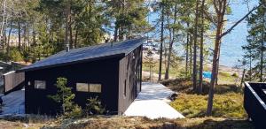 Ein schwarzes Gebäude im Wald neben dem Wasser. in der Unterkunft Kvarnsands Strandstugor / Kvarnsand Beach Lodges in Grisslehamn