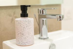 a white soap bottle sitting on a sink next to a faucet at KASA ZEN - Climatisation - Tout équipé - Stationnement gratuit in Saint-Chamond