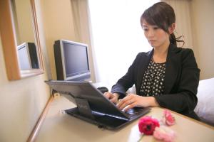 una mujer sentada en un escritorio usando un ordenador portátil en Heiwadai Hotel Tenjin, en Fukuoka