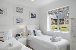 two beds in a white bedroom with a window at The Hawthorns in Polzeath