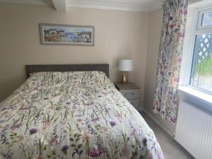 a bedroom with a bed with a floral bedspread and a window at Primrose Steps in Goodrington