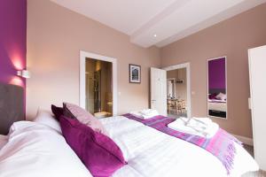 um quarto com uma grande cama branca com almofadas roxas em The Spires Serviced Apartments Edinburgh em Edimburgo