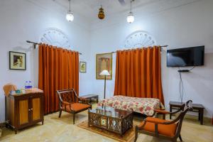 Schlafzimmer mit orangefarbenen Vorhängen, einem Bett und einem TV in der Unterkunft Neemrana's - Deo Bagh in Gwalior