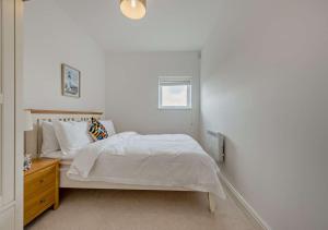 a white bedroom with a bed and a wooden dresser at Bayview Apartment - Machynys in Llanelli