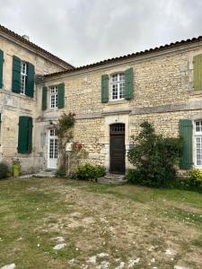 un antiguo edificio de piedra con persianas verdes y una puerta en Maison Garesché, en Nieulle-sur-Seudre