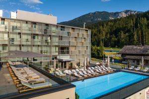 a hotel with a swimming pool and lounge chairs at Arena Franz Ferdinand Nassfeld in Tröpolach