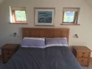 um quarto com uma cama com duas mesas de cabeceira e duas janelas em The Neuk Achmore Plockton em Stromeferry