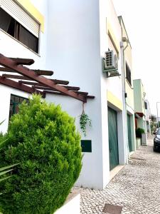 a white building with a green bush next to a building at Caparica Coast Townhouse Apartments in Charneca
