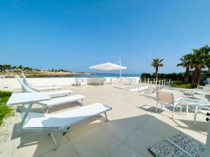 a patio with white tables and chairs and the beach at Torre Pozzillo Beach in Cinisi