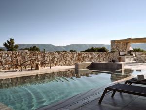 a swimming pool with chairs and a stone wall at Onore Villa, Featuring Heated Pool, By ThinkVilla in Gaïtánion