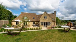 Warren House and Spa boutique Cotswold stay في سيرنسيستر: منزل كبير مع ساحة مع اثنين من المراجيح الخشبية الكبيرة