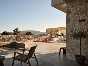 un patio con tavolo, sedie e parete in pietra di Onore Villa, Featuring Heated Pool, By ThinkVilla a Gaïtánion
