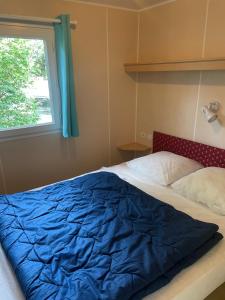 a bed with a blue comforter and a window at Domaine Camping les Roches in Le Crestet