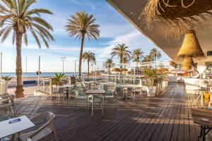 ein Restaurant mit Tischen und Palmen am Strand in der Unterkunft Meraki Beach Hotel - Only Adults in Playa Pobla de Farnals