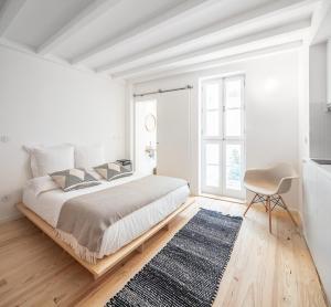 a white bedroom with a large bed and a chair at Loureiro 59 in Coimbra