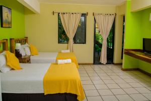 two beds in a room with green walls and a tv at Banana Palms Hotel in Río Dulce