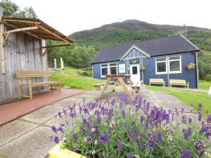 a blue house with a bench and purple flowers at West Highland Lodge in Kinlochleven