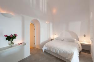 a white bedroom with a bed and a vase of flowers at Evmenia Luxury Cave Villa in Oia