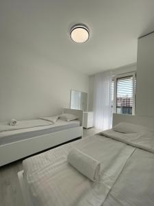 a white bedroom with two beds and a lamp at Gega Apartments in Gjakove