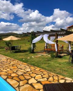 un patio con mesas y sombrillas junto a una piscina en Chalés para temporada - Chalés Apuã - 500 metros da Cachoeira, en Carrancas