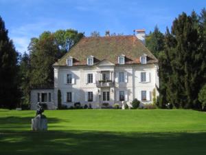 une grande maison blanche au-dessus d'un champ verdoyant et luxuriant dans l'établissement Hôtel des Trois Rois, au Locle