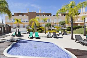 a swimming pool with chairs and umbrellas and a building at Cabanas Gardens by MY CHOICE in Cabanas de Tavira