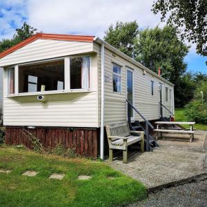 uma pequena casa branca com um banco e uma mesa em Hedgehog Holiday Home in the countryside, 10 mins to Lligwy beach em Llandyfrydog