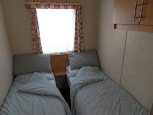 Duas camas num pequeno quarto com uma janela em Hedgehog Holiday Home in the countryside, 10 mins to Lligwy beach em Llandyfrydog