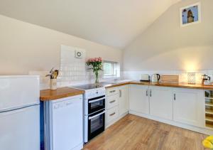 a white kitchen with white appliances and wooden floors at Tui Cottage in Snape