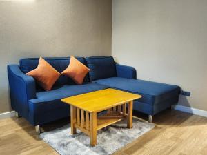 Sofá azul con almohadas de color naranja y mesa de madera en Baan Nonzee Condo en Bangkok