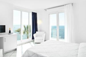 a white bedroom with a bed and a chair and windows at Villa Grachira in Fertilia