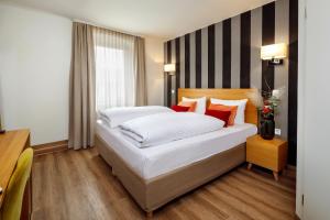 una camera da letto con un letto con lenzuola bianche e cuscini rossi di Hotel am Peterstor a Ratisbona